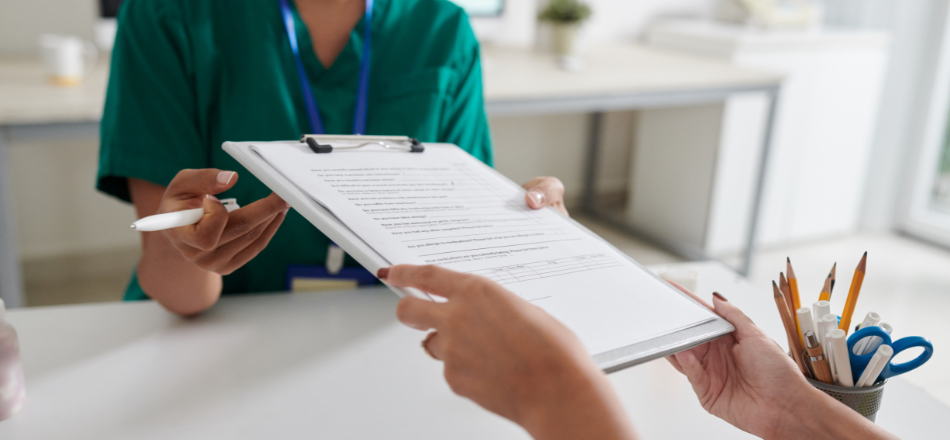 A zoomed-in photo of a patient handing a paper questionnaire to a healthcare professional wearing green scrubs