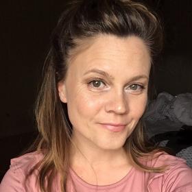 woman with brown hair smiling in a pink shirt