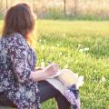 woman looking off over a green field writing