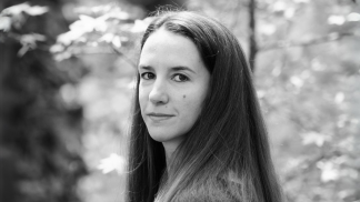 A grayscale photograph of a woman with dark hair standing in front of a nature scene