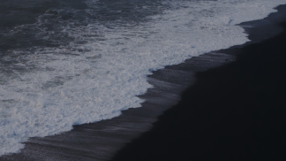 A grayscale photo of an ocean wave hitting sand