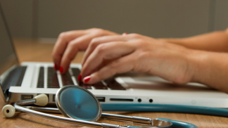 Hands typing on laptop with stethoscope