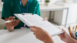A zoomed-in photo of a patient handing a paper questionnaire to a healthcare professional wearing green scrubs