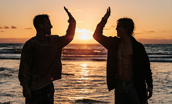 Two men in front of sunset sea giving hi fives.